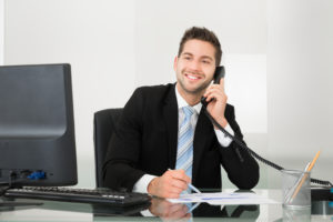 Young businessman discussing over documents on telephone at desk in office